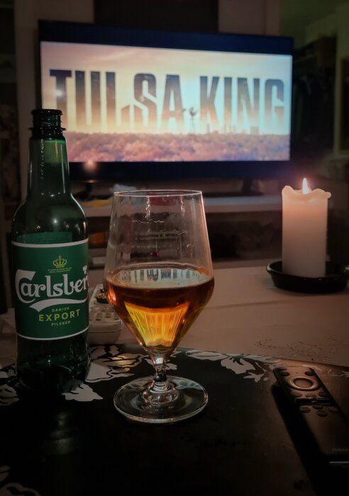 En ölflaska, glas med öl, och stearinljus framför en TV som visar "Tulsa King".