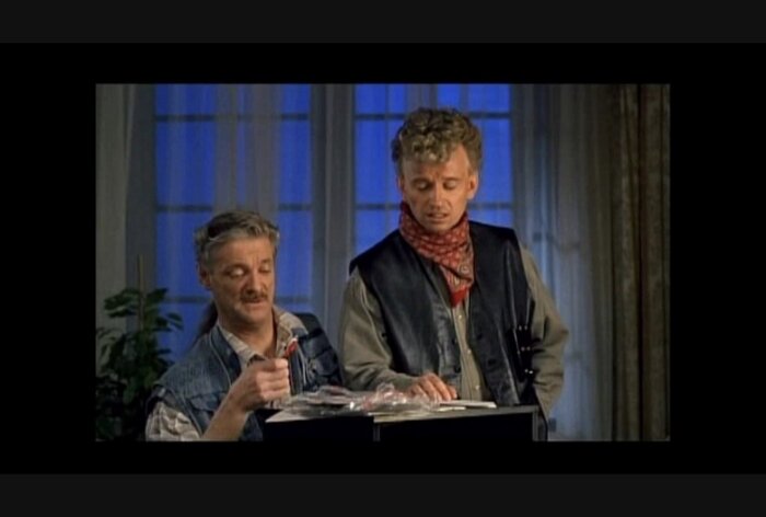 Två personer i cowboykläder står inomhus vid ett bord. Den ena håller i ett föremål.