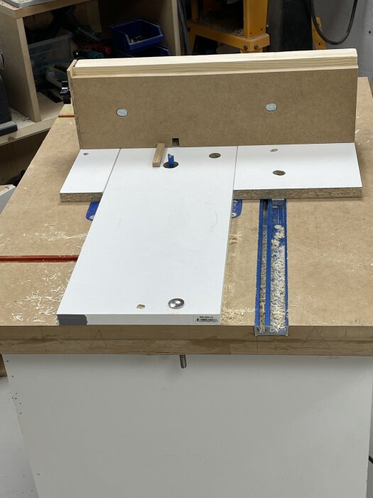 Fräsbord med fingerskarvsjigg monterad, omgiven av träspån, i ett snickeri med verktyg i bakgrunden.