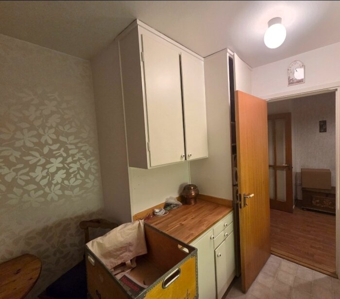 Gammalt kök med vita skåp, träbänk och öppen dörr, del av ett renoveringsprojekt.