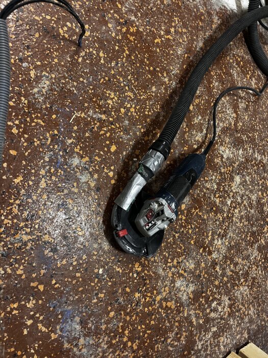Betongslip placerad på ett brunmönstrat golv, omgiven av dammsugarslang, redo för slipning.