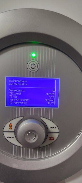 Närbild på en värmepumps display med blått skärmljus, som visar temperatur och driftinställningar, samt en grönt lysande strömbrytare.