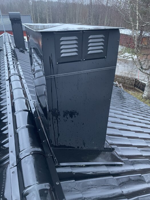 Ventilationshuv i svart metall på ett plåttak med tecken på fukt och en möjlig läcka upptäcktes.