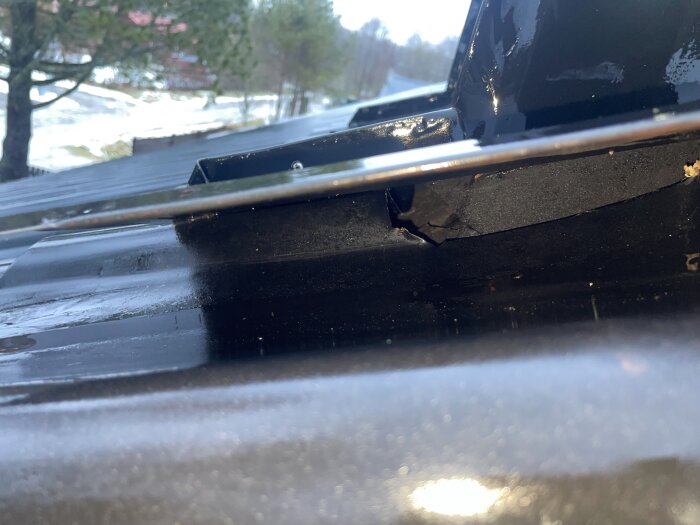 Närbild av ett hål under en ventilationshuv på ett plåttak, möjligen orsaken till läckage, synlig blöt råspont runt omkring.