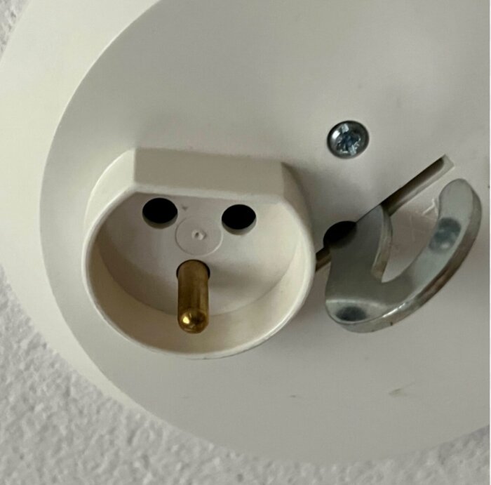 Rund elkontakt med stift för lampa, monterad på vit väggplatta.