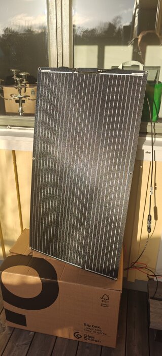 Solpanel lutad mot ett fönster, stående på en kartong i novemberljus.