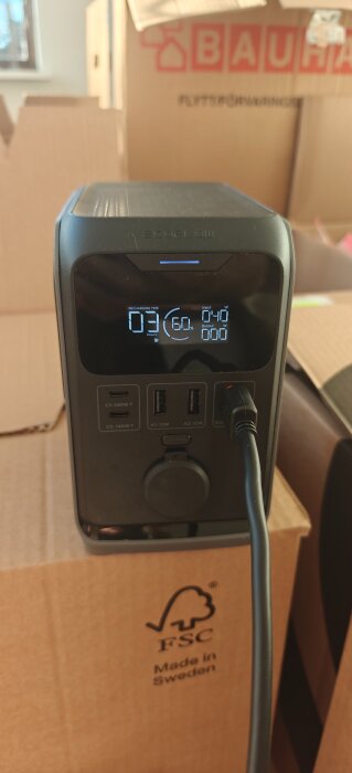 Bärbar elstation på kartong. Display visar 60% laddning, 3 timmar kvar. Används för att testa solpanelers effektivitet i novemberljus.