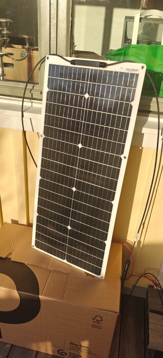 Solpanel lutad mot en vägg i solljus, placerad på en kartong. Novembertest av solpanelens effektivitet.