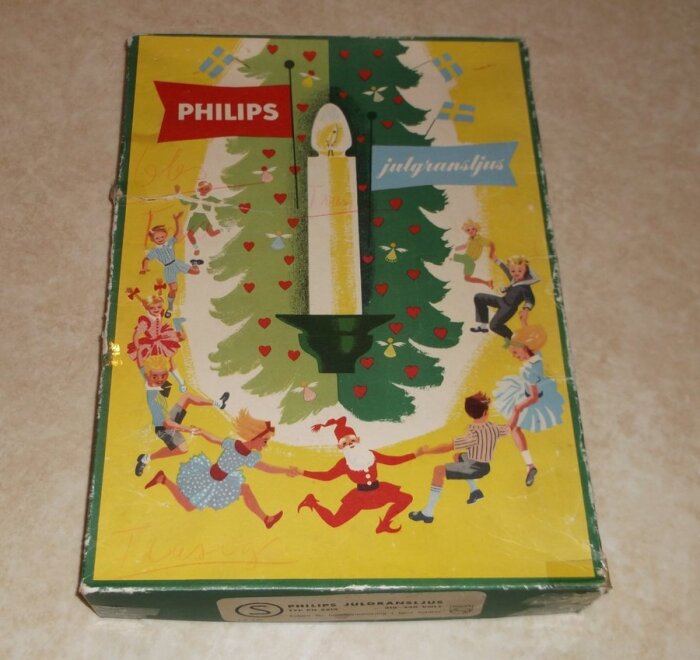 Förpackning av Philips julgransljus från 1960-talet med illustration av barn och jultomte dansande runt en gran.