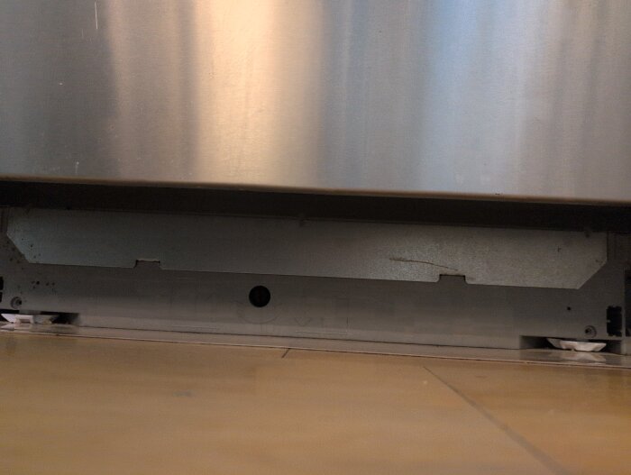 Undersidan av en diskmaskin med borttagen sockelplåt. Man ser en mindre plåt bredvid sockeln och en skruv med torx 20 på insidan.