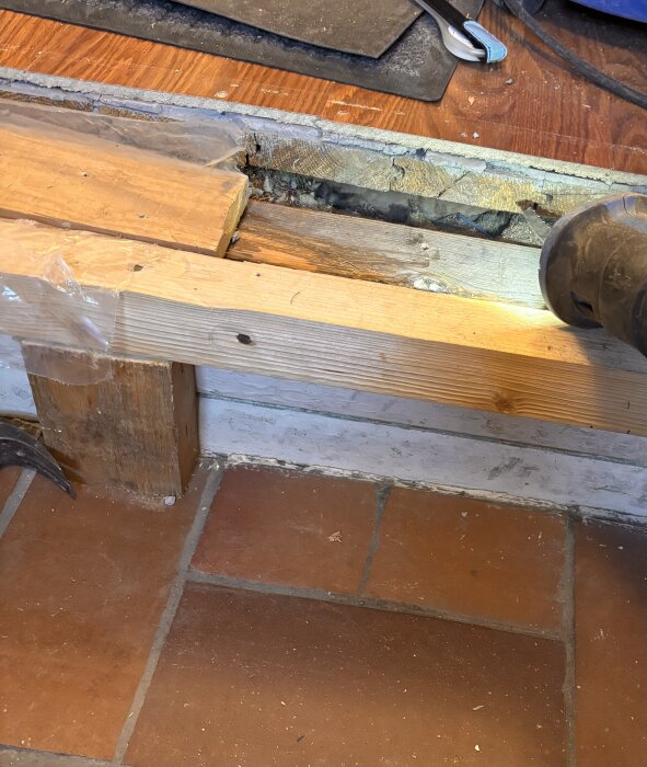 Träreglar och en skadad parkettdel övergår till terrakottafärgad klinker, med verktyg och byggmaterial i bakgrunden.