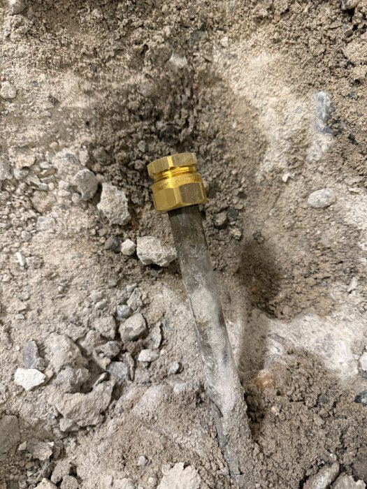 Ett stålskvallerrör i grov cementmiljö, delvis exponerat vid golvbrunnen, med gul mässingskoppling synlig.