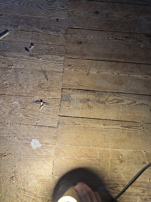 Golvgeneralskarv framför trappavsats, olika typer av brädor synliga, vissa av god kvalitet, andra som råspont. Person håller ficklampa.