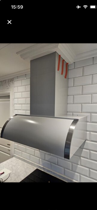 Köksfläkt installerad på köksväggen med vitt kakel, utan galler i toppen av skorstenen för utblås.