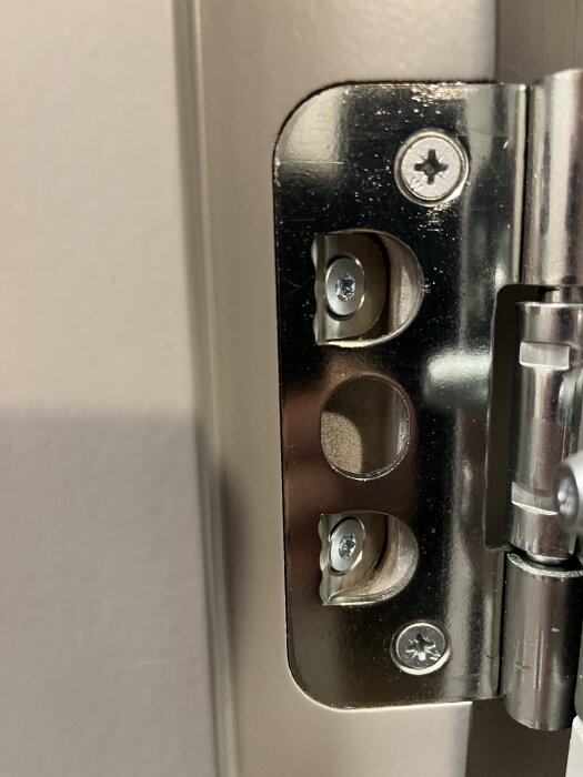 Närbild på en metallgångjärn och skruvar i en branddörr, med skruvarna i olika färger för justering.