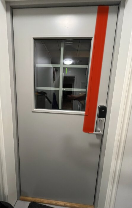 Grå branddörr med glasruta och dörrhandtag, röd markering visar var dörren skaver.