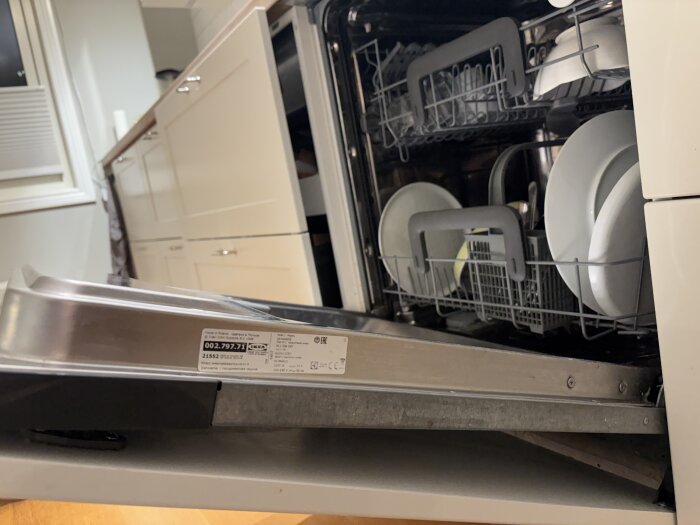Diskmaskin med öppen lucka visar tallrikar och bestick inuti, fokus på fronten som verkar fäst vid diskmaskinsdörren.