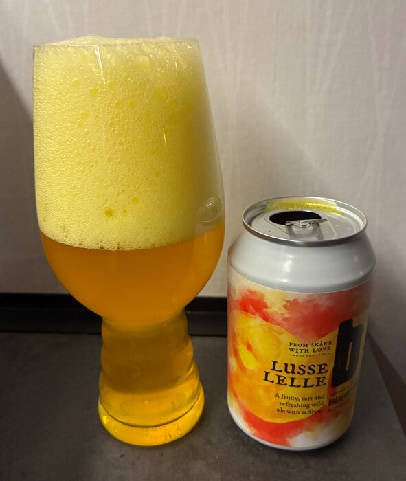 Ett glas gyllengul öl med mycket skum bredvid en burk märkt "Lusse Lelle" med färgglad etikett.