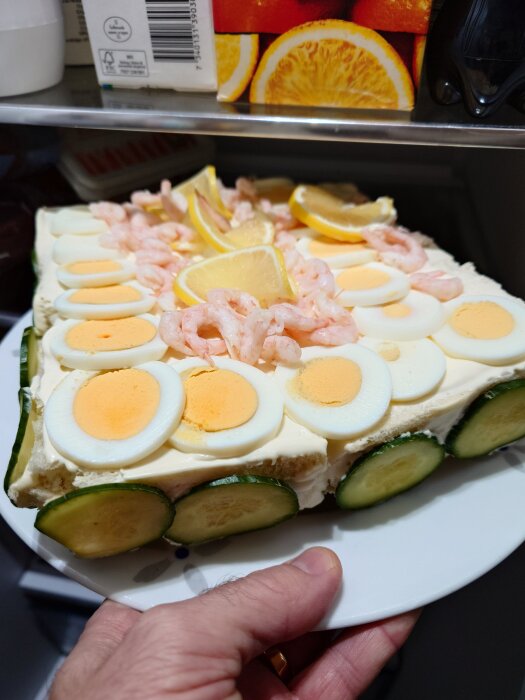 Smörgåstårta med ägg, räkor, citron och gurka i ett kylskåp.