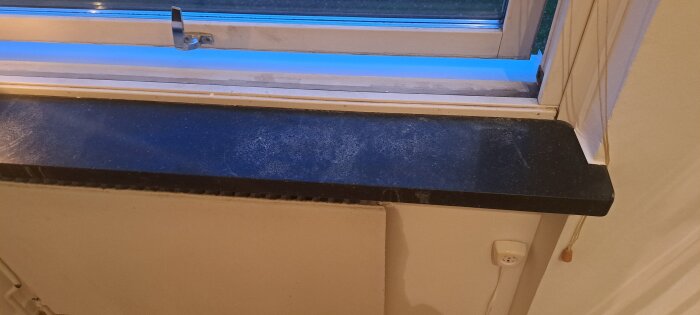 Vindueskarm med hvide mærker fra blomsterpotter, muligvis marmor eller sten, set i et boligrum med delvis åben vindue og snortrukket rullegardin.