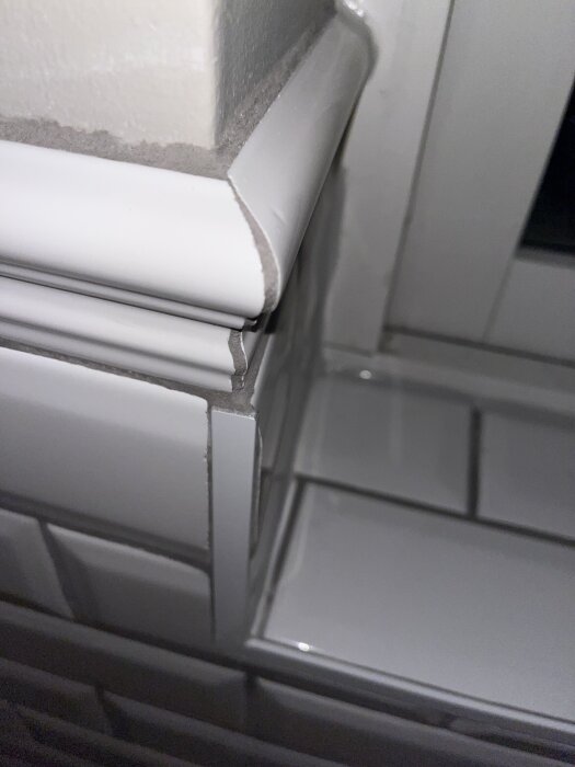 Närbild av kakel i hörn med ojämna fogar och en ful list vid fönstret, samt mörkare fogfärg än avsett i badrum under renovering.