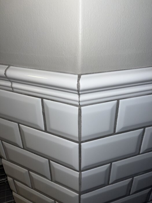 Närbild av kakelfogar där hörnet visar ojämna linjer och mörk fog mot vit kakel i ett badrum.