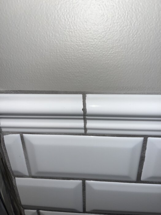 Kakelsättning i badrum med sandgrå fogar, synliga ojämnheter och ofördelaktig listanvändning.