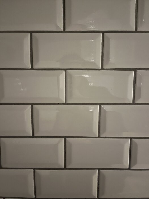 Vita kakelplattor med mörkare fogar, ojämna skarvar och slarvigt utförda vinklar visar problem med kakelsättningen i ett badrum.