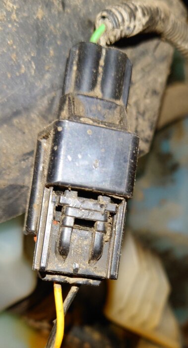 Närbild på en elektrisk kontakt med synlig låsmekanism framtill och lösa kopplingskablar i en dammig miljö.