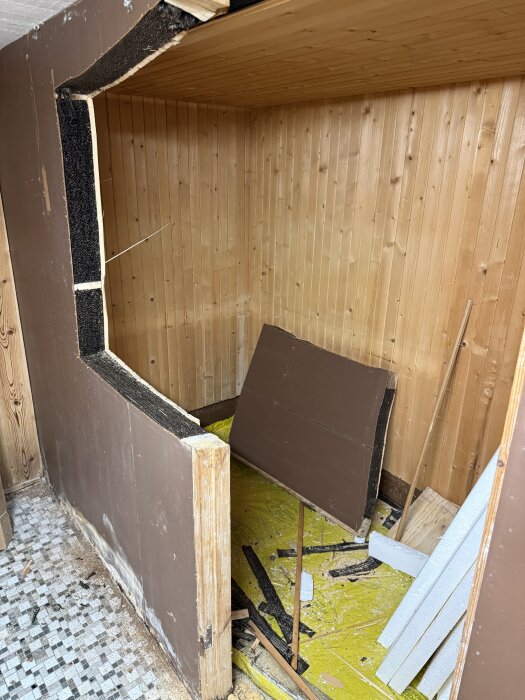 Rivet rum med brun träpanel och trasigt material på golvet, tidigare använd som bastu.