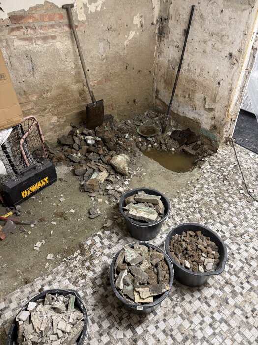 Rivet källargolv med ficka av vatten, omgivande murkna betongbitar i hinkar och verktyg i ett gammalt hus från 1947.