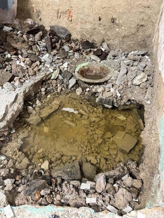 Vattenansamling under gammal duschplatta i källaren; synlig grov sand och stenkross efter rivning av möglig bastu och dusch.