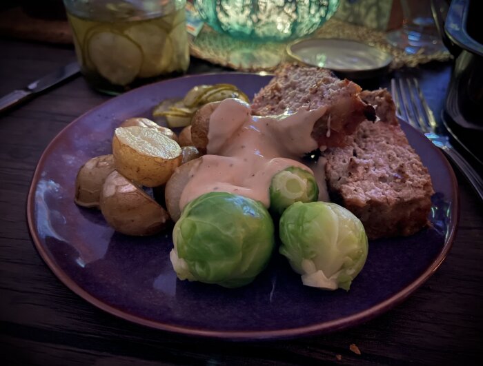 Tallrik med köttfärslimpa, brysselkål, skivad potatis och inlagd gurka, toppat med gräddsås.