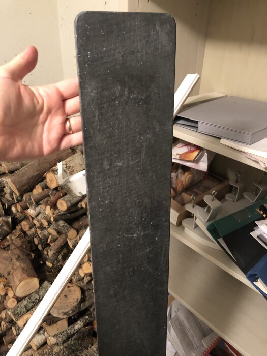 Eternitcementfönsterbräda hålls upp, med hyllor och ved i bakgrunden.