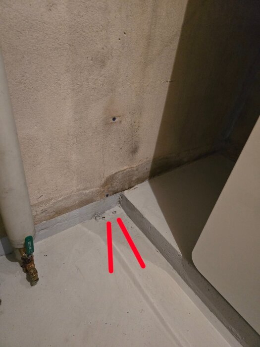 Fuktfläckar på betongvägg i pannrum, med rör och märkning på golvet.