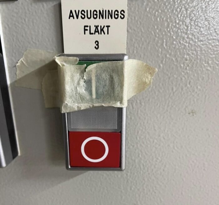 Röd knapp märkt "Avsugnings fläkt 3" med tejp över, på en maskinpanelel.