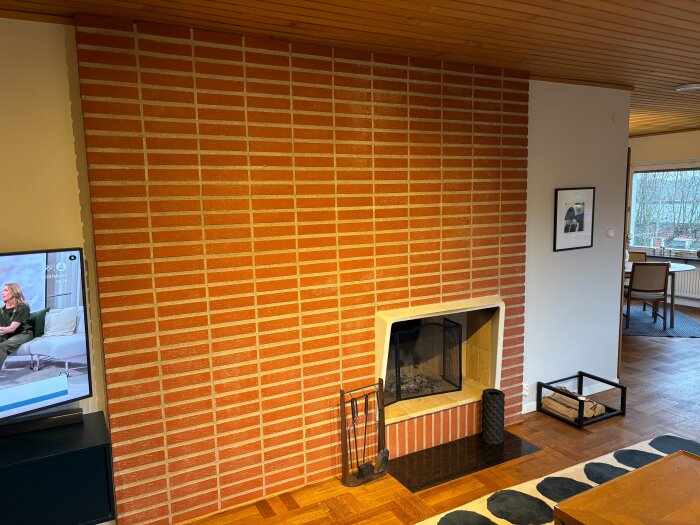 Öppen spis från 1963 med rödtegel och en svart eldstadsbädd i en ljus vardagsrumsmiljö med trägolv och tak.