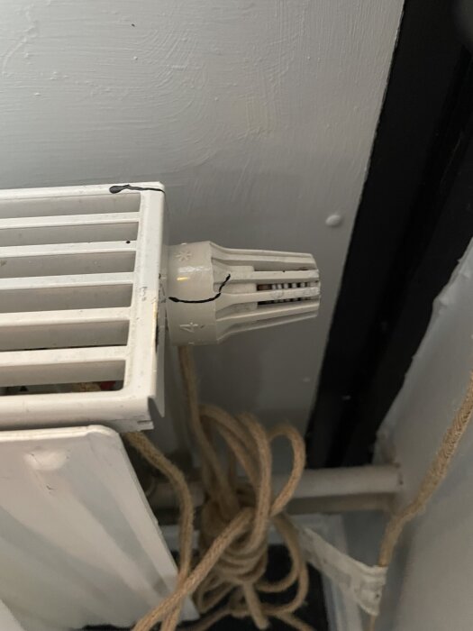 Radiator med en termostatventil monterad, omgiven av ett snöre.