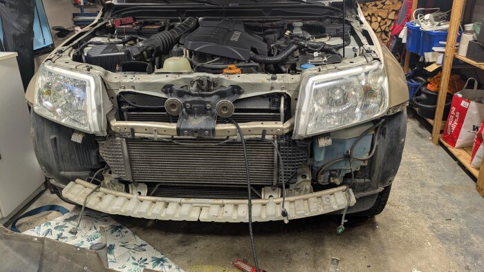 Bil med avlägsnad front i garage, visar motor och komponenter under byte av spolarvätskepump.