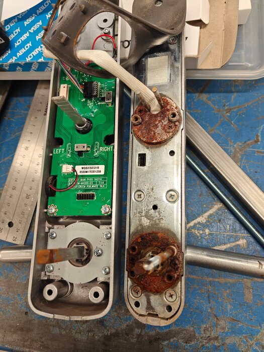 Isärmonterat Yale Doorman V2N med rostiga delar och kretskort synligt. Bakgrund av verktyg och arbetsbord.