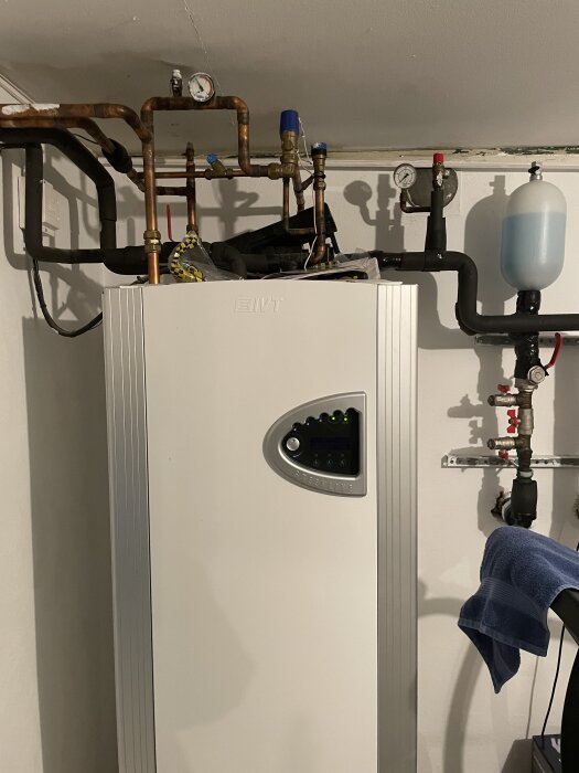 Värmepump med kopparrör och en blå tryckbehållare, omgiven av isolerade slangar. Fråga om byte av igenkloggade slangar.