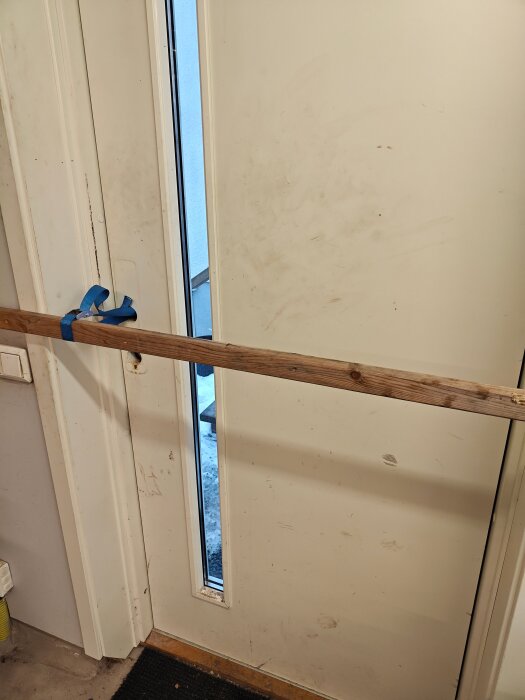 Trädörr med ett långt fönster förstärkt med en träregel och blå spännrem.