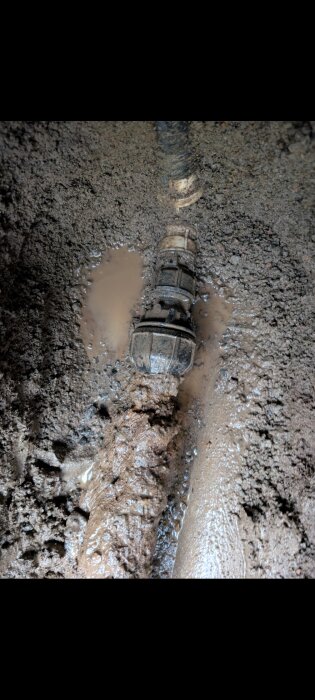 Ett rör med koppling i jordigt område med vattenpöl, visar en potentiell läcka och kopplingsdetaljer.