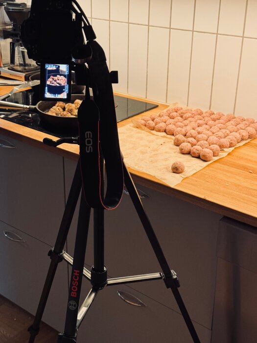 Stativ från Bosch fotograferar köttbullar på en köksbänk; bild av en kamera pekande mot stekpanna och köttbullar på bakplåtspapper.