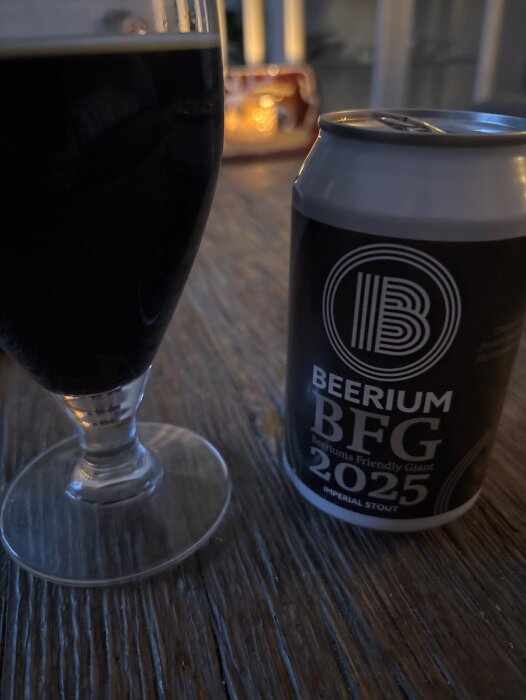 Burk och glas med Beerium BFG 2025 stout på ett träbord, med ett ljus i bakgrunden.