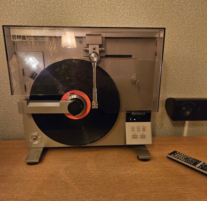 Stående tangentialspelare från 1981 med vinylskiva på plats, uppställd på ett träbord med en fjärrkontroll bredvid.