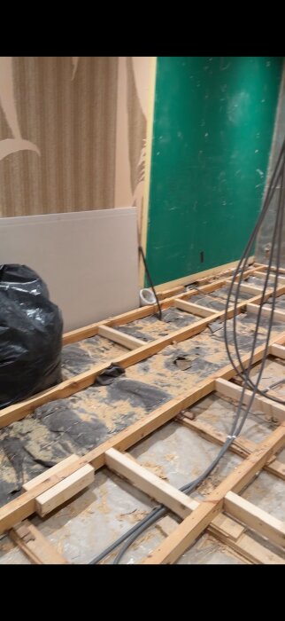 Uppreglat golv med blottad isolering och kablar, plast täcker betongplattan i pågående sovrumsbygge.
