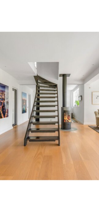 Rak trappa utan ledstång inomhus, bredvid en kamin, med svängd form mot övervåningen i modernt renoverat hus.