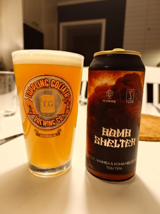 En ölburk med etiketten "Bomb Shelter" från Nurme och ett glas fyllt med ljus öl, står på ett bord.