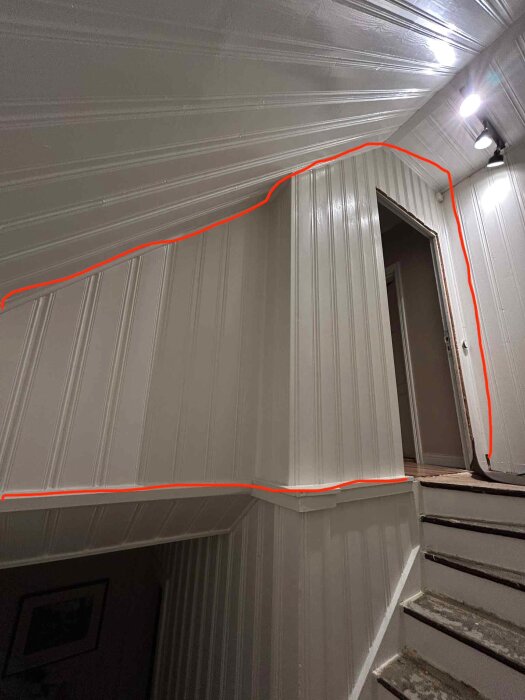 Vinklad trappa inomhus med vit träpanel, markerad med röd linje som föreslår borttagning av väggen mellan trappan och hallen.